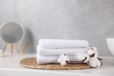 Temiz havlu yığını, pamuk çiçekleri ve beyaz masadaki ayna, yakın plan.