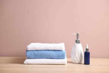 Temiz havlular ve kozmetik ürünleri bej arka plana karşı ahşap masaya yığılmış.