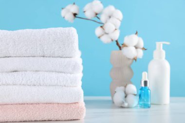 Temiz havlular, pamuk çiçekleri ve kozmetik ürünleri beyaz mermer masa üzerinde açık mavi arka plan, yakın çekim