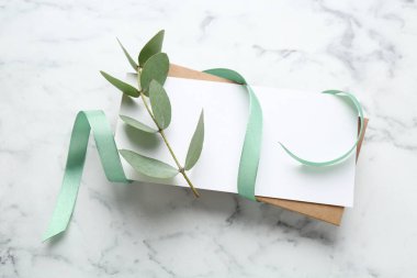 Beyaz mermer zemin üzerinde boş kart, kurdele ve okaliptüs dalı, düz yatıyordu