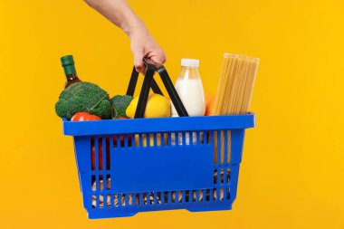 Sarı arka planda farklı ürünleri olan alışveriş sepeti tutan adam, yakın plan.