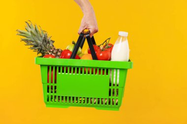 Sarı arka planda farklı ürünleri olan alışveriş sepeti tutan adam, yakın plan.