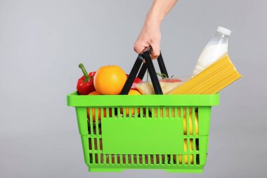 Elinde gri arka planda farklı ürünler olan alışveriş sepeti tutan adam, yakın plan.