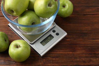 Elektronik mutfak terazisi ve ahşap masada bir kase yeşil elma, yakın plan. Metin için boşluk