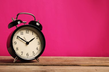 Parlak pembe arkaplan ile ahşap masa üzerinde bir siyah alarm saati, metin için boşluk