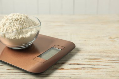 Modern electronic kitchen scale with bowl of flour on wooden table, closeup. Space for text