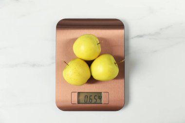 Modern elektronik mutfak terazisi, beyaz mermer masa üzerinde elmalar, üst manzara.