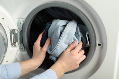 Kadın çamaşır makinesine kot pantolon koyuyor, yakın plan.