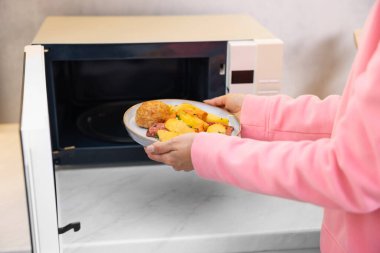 Kadın tabağı mikrodalgaya koyuyor, yakın plan.