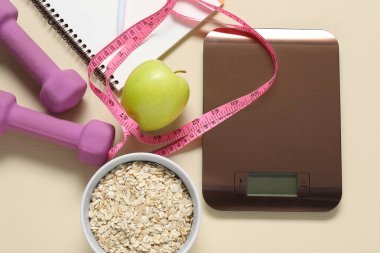 Elektronik mutfak terazisi, mezuralar, dambıllar, not defterleri ve bej masadaki ürünler, düz yatak. Kalori kontrolü