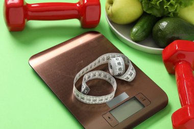 Elektronik mutfak ölçeği, mezura, açık yeşil arka plandaki dambıl ve ürünler, yakın plan. Diyet