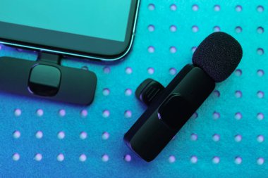 Lavalier mikrofon ve kablosuz alıcısı olan akıllı telefon neon ışıklarda, düz yatıyordu.