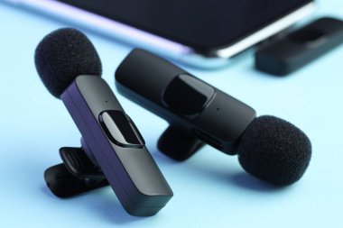 Açık mavi arkaplanda kablosuz alıcısı olan Lavalier mikrofonlar ve akıllı telefon.