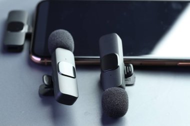 Açık gri arkaplanda Lavalier mikrofonlar ve akıllı telefon, yakın plan.
