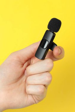 Sarı arka planda lavalier mikrofon tutan kadın, yakın plan.