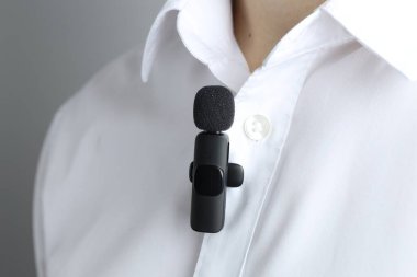 Gri arka planda gömleğine mikrofon takmış bir adam.