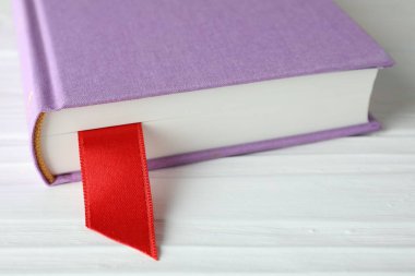 Beyaz ahşap masa üzerinde kırmızı kurdele yer imi olan kitap, yakın plan.