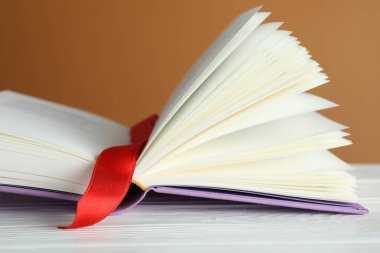 Kahverengi arkaplana karşı beyaz ahşap masa üzerinde kırmızı kurdele yer imi olan kitabı aç, kapat