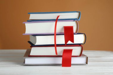 Kahverengi arkaplana karşı beyaz ahşap masa üzerinde kırmızı kurdele yer imleri olan kitaplar, yakın plan