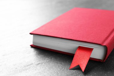 Koyu desenli masa üzerinde kırmızı kurdele yer imi olan kitap, yakın plan.