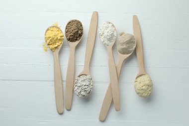 Beyaz ahşap masadaki kaşıklarda farklı türde un, düz.