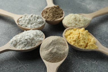 Gri masadaki kaşıklarda farklı türde un, yakın plan.