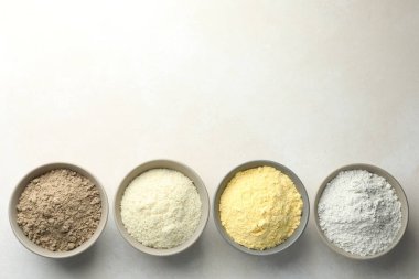 Açık gri masadaki kaselerdeki farklı un türleri, düz yatış. Metin için boşluk