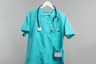 Steteskop ve rozetli sağlık çalışanı üniforması gri arka planda.