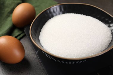 Gri masadaki şeker ve diğer ürünlerle birlikte dijital mutfak terazisi, yakın plan.