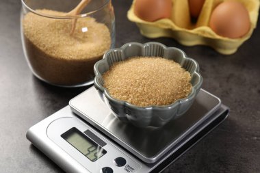 Dijital mutfak terazisi, kahverengi şeker kasesi ve gri masadaki diğer ürünler, yakın plan.