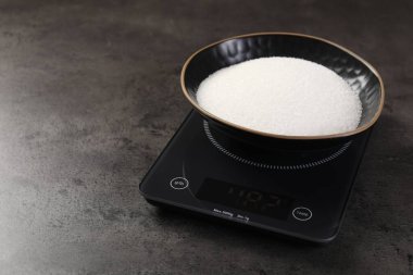 Dijital mutfak terazisi ve gri masada bir kase şeker, yakın plan. Metin için boşluk