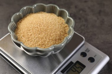 Dijital mutfak terazisi, gri masanın üzerinde kahverengi şeker kasesi, yakın plan.