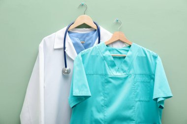 Açık yeşil arka plandaki askılarda steteskop olan sağlık çalışanları üniformaları.