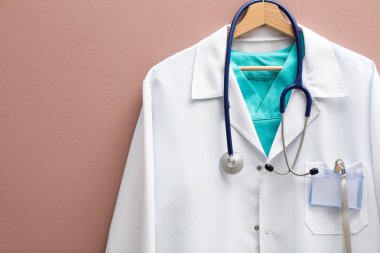 Doktor ceketi, steteskop ve rozeti bej arka planda asılı. Metin için boşluk
