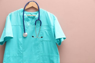 Bej arka planda steteskop takılı sağlık çalışanı üniforması. Metin için boşluk