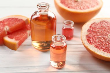 Aromatik esanslı parfüm şişelerini aç ve beyaz ahşap masada greyfurt dilimleri, yakın plan.