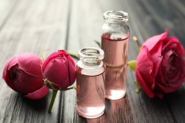 Aromatik esanslı parfüm şişelerini aç ve gri ahşap masada güller, yakın plan.