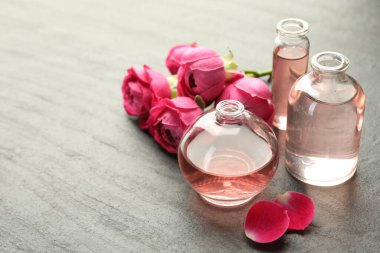 Gri desenli masa üzerinde aromatik esanslı yağlar ve güllerle parfüm şişelerini açın. Yakın plan. Metin için boşluk