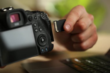 SD bellek kartını masadaki fotoğraf makinesine yerleştiren adam, kapat