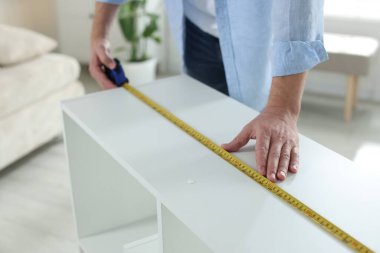 Beyaz rafları bantla ölçen adam içeride, yakın plan.