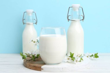 Taze süt ve çiçekler beyaz masada açık mavi arka planda