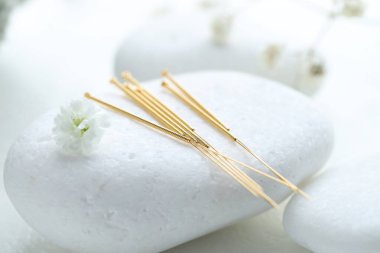 Beyaz arka planda akupunktur iğneleri, çakıl taşı taşı ve çiçek tomurcukları, yakın plan