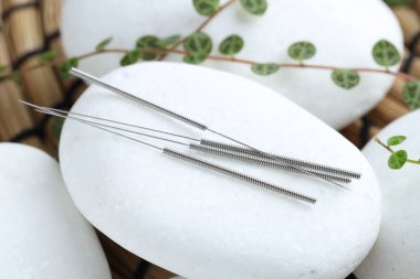 Akupunktur iğneleri, spa taşları ve hasırın üzerindeki yapraklar, yakın plan.