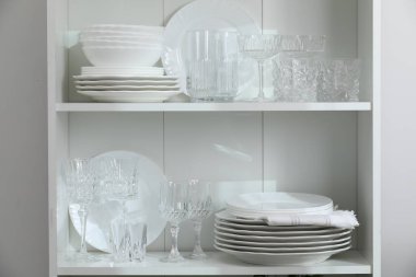 Beyaz duvarın yanındaki raflarda temiz bardaklar ve tabaklar.