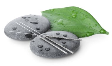 Akupunktur iğneleri, ıslak spa taşları ve beyaza izole edilmiş yaprak.