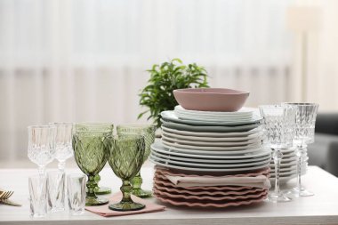 Beyaz ahşap masada temiz bardaklar, tabaklar ve yeşil bitkiler.