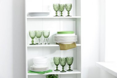 Beyaz duvarın yanındaki raflarda temiz bardaklar ve tabaklar.