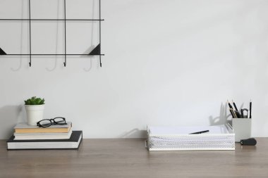 Farklı kırtasiye malzemeleri, çiçek dekoru ve beyaz duvarın yanındaki ahşap ofis masasında gözlük.