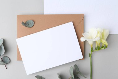 Boş tebrik kartı, kağıt zarf, çiçek ve okaliptüs yaprakları açık gri arka planda, düz uzanmış