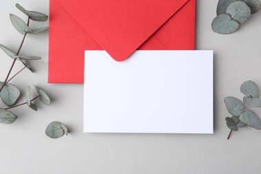 Boş tebrik kartı, kağıt zarf ve okaliptüs yaprakları açık gri arka planda, düz yatıyordu.
